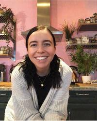 Photograph of Ashlea Cromby smiling in a kitchen with lots of houseplants behind her